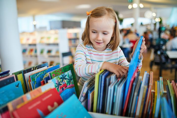 Et barn ser gjennom fargerike bøker i et bibliotek.
