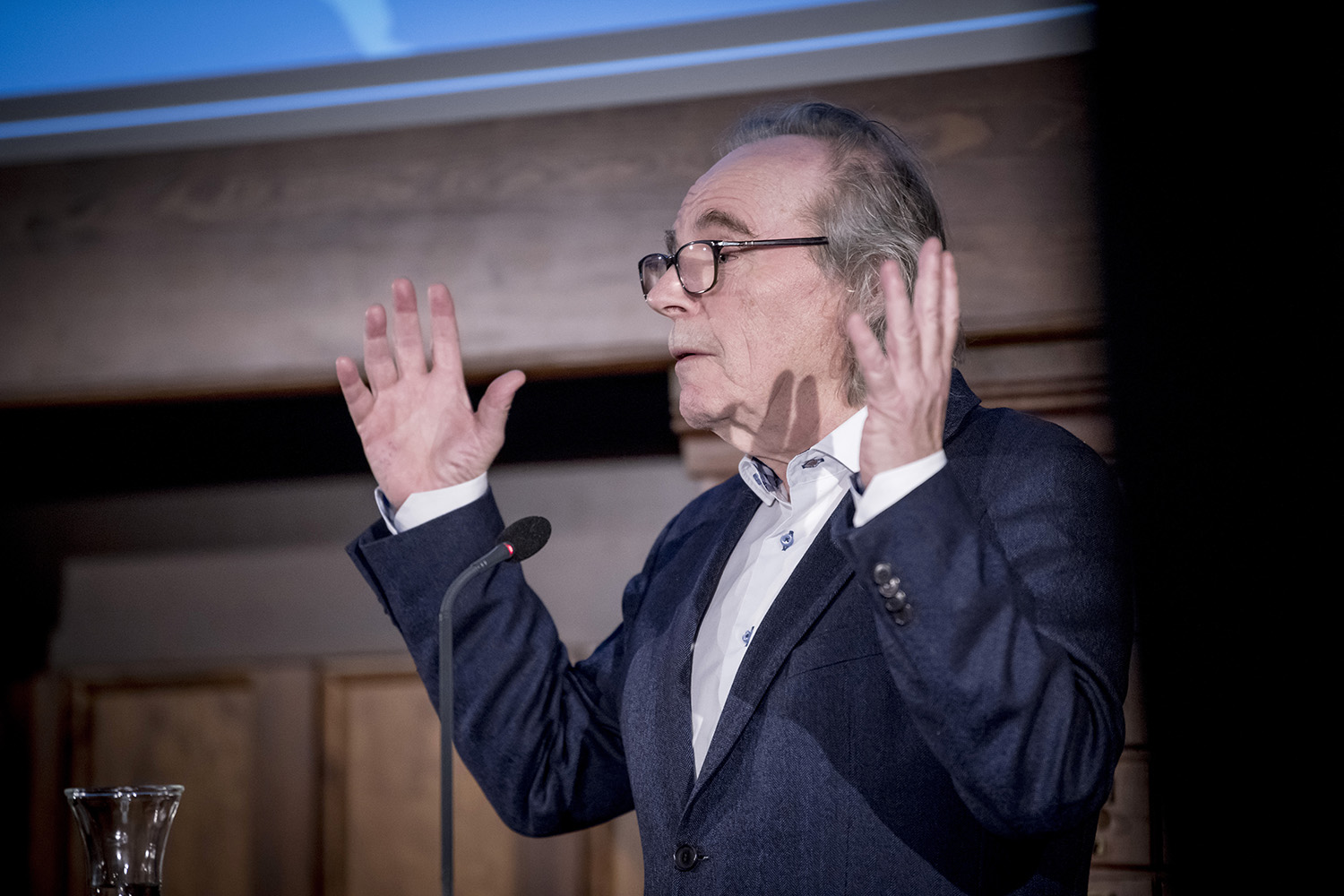 En mann med briller gestikulerer mens han holder foredrag ved en talerstol på Nasjonalbibliotekets scene.