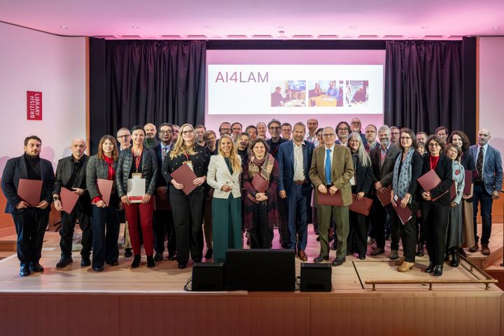 A group of people standing on a stage, holding certificates. A screen in the background displays "AI4LAM."