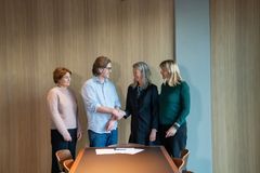 Personer i et møterom står ved et bord og håndhilser.