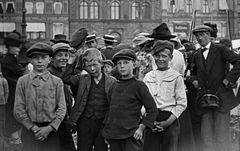 Svart-hvitt bilde av en gruppe gutter i eldre klær som ser mot kameraet, med flere andre personer i bakgrunnen.