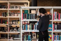 En person leser en bok ved bokhyllene på Lambertseter bibliotek.