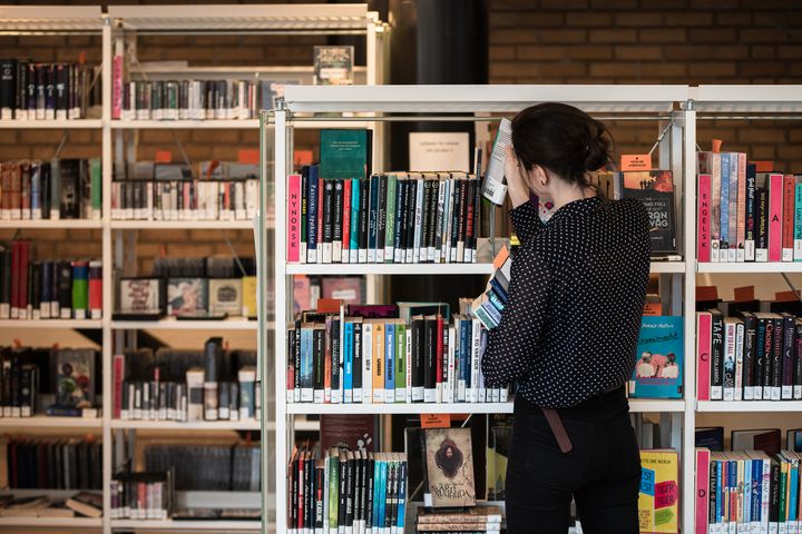 En%20person%20leser%20en%20bok%20ved%20bokhyllene%20p%E5%20Lambertseter%20bibliotek.