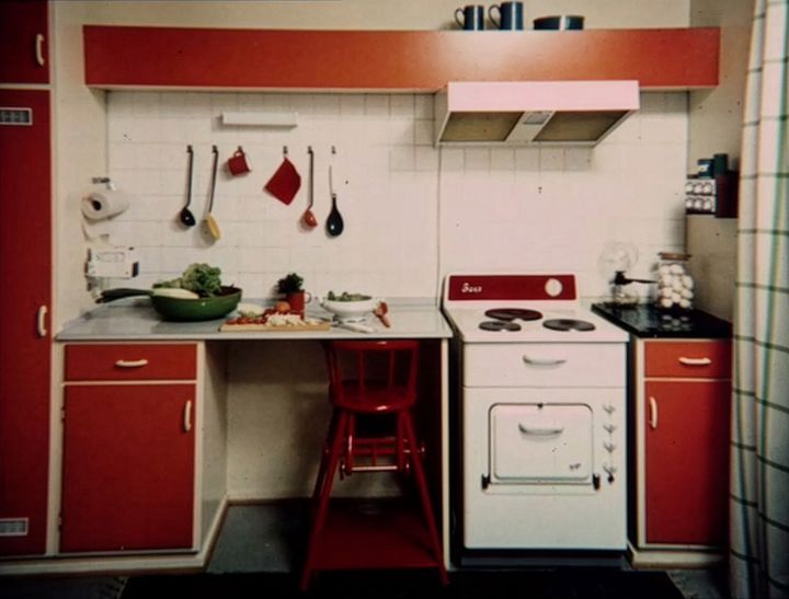 Rødt og hvitt retro kjøkken med komfyr, gryter og grønnsaker på benken.