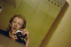 Selvportrett i speil av mann med rufsete hår som fotograferer med kamera.