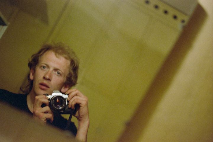 Selvportrett i speil av mann med rufsete hår som fotograferer med kamera.