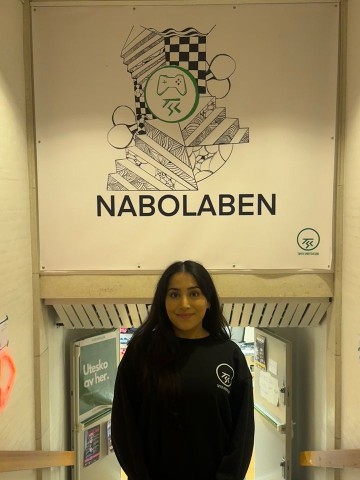 Portrett%20av%20Halima%20Faisel%20Butt%20under%20et%20skilt%20der%20det%20st%E5r%20Nabolaben