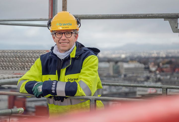 Administrerende direktør i Bravida, Tore Bakke, står på taket av en bygning under oppføring. Byggeplass. Tore smiler og er kledt i verneutstyr.