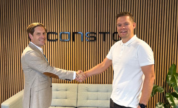 SAMARBEID Eirik Helgøy, avdelingsleder i Bravida, og Endre Kristiansen, prosjektsjef i Consto tar hverandre i hånden og smiler til kamera ved kontraktssigneringen. Constos logo i bakgrunnen.