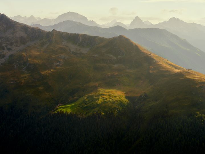 Et mektig fjellplatå i Davos med mange topper og lys himmel og sola som skinner ned i dalen.