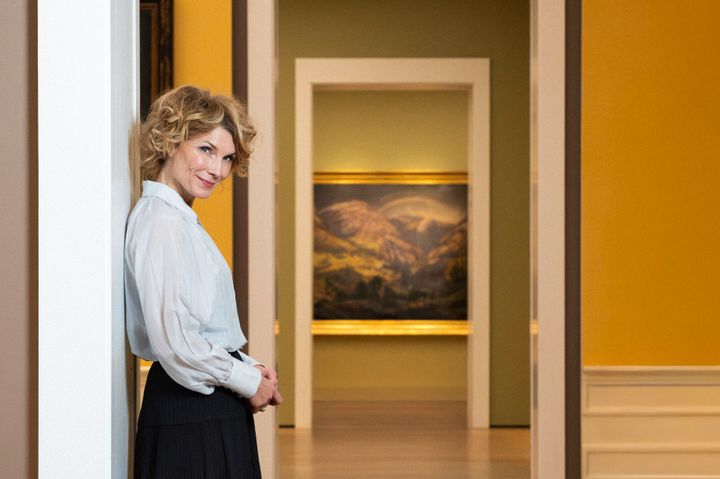 Foto av Herborg Kråkevik, lent mot en dørkarm i utstillingssalene i Nasjonalmuseet.