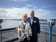 En kvinne og en mann står på en balkong med havutsikt i bakgrunnen.