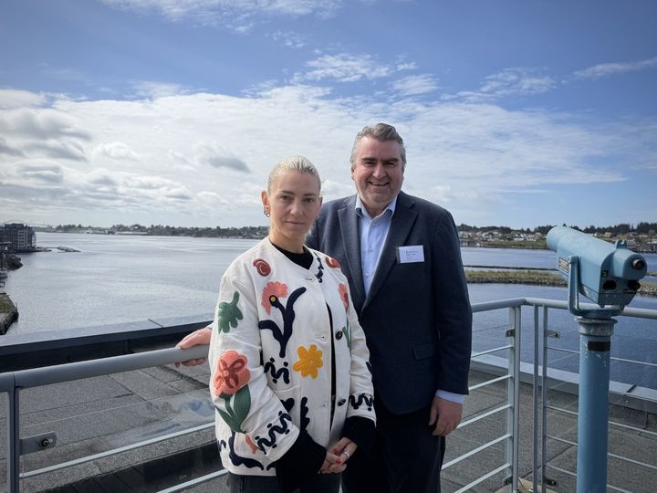 En kvinne og en mann står på en balkong med havutsikt i bakgrunnen.