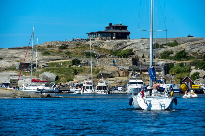Seilbåter og motorbåter i en travel båthavn ved svaberg en sommerdag.