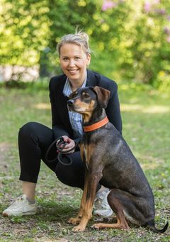 En kvinne smiler mens hun sitter ute med en stor, brun hund.