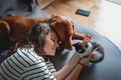 Kvinne koser med en hund og en kattunge på en sofa.