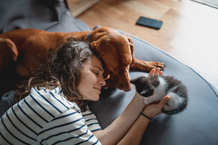 Kvinne koser med en hund og en kattunge på en sofa.