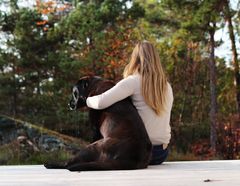 En person sitter tett inntil en hund på en terrasse, omgitt av høstfargede trær.