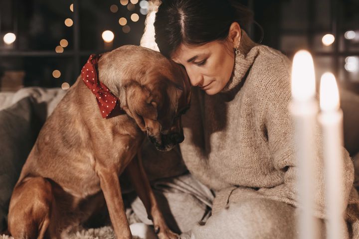 En kvinne sitter ved siden av en hund som ser engstelig ut. Hunden har på seg en rød sløyfe.