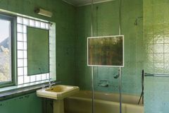 The interior of a bathroom in green tiles, a photograph og a damp window placed in front of the bathtub.