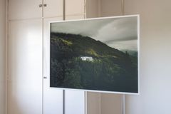 Photography of a green mountain landscape in the western part of Norway, showing a glimpse of Luster sanatorium, the picture is placed in front of a wall.