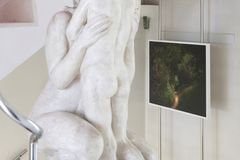 A photograph of a stairwell with a picture of a green path in Davos and a sculpture of mother and child placed on the left.