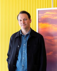 Portrait of artist Espen Gleditsch in front of a bright yellow wall and a small part of his photography "Sunrise".