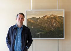 Portrait of artist Espen Gleditsch beside his photograpy of a mountain landscape with a tuberculosis sanatorium to the lower left.