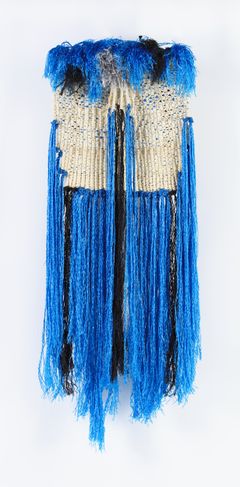 Large tapestry in a bright blue colour made by wool, sisal, plastic and paper. The bright coloured strips are hanging down.