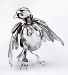 A bird made of cutlery where spoons form the head, body and wings and forks are the legs and claws.