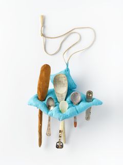 A turquoise pillow made of ceramics with spoons put inside, and a thread to be worn around the neck as a necklage.