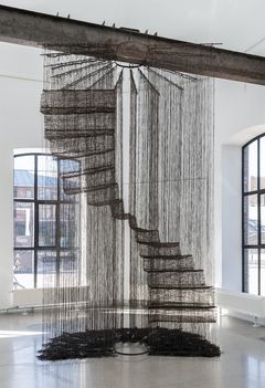 A large staircase made by black threads hanging from a beam in the ceiling.