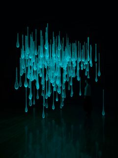 Turquoise drops of glass against a black background, mirroring itself in the lower part of the picture.