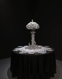 Tiny pieces of porcelain are pieced together in a mushroom like installastion, placed on a table with a black table cloth.