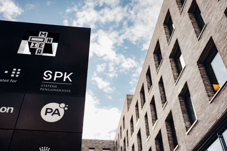 Skilt med SPK – Statens pensjonskasse – foran en moderne kontorbygning, med blå himmel i bakgrunnen.