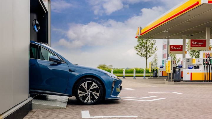 Bil i en batterbyttestasjon og en bensinstasjon.