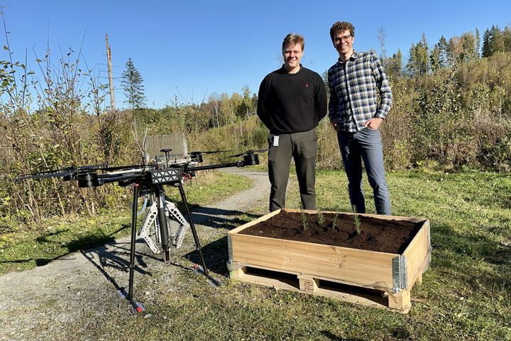 To menn står ved siden av en stor drone og en trekasse med planter.