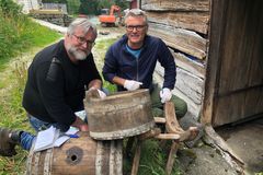 To menn arbeider med gammelt bryggeutstyr ved et trehus.