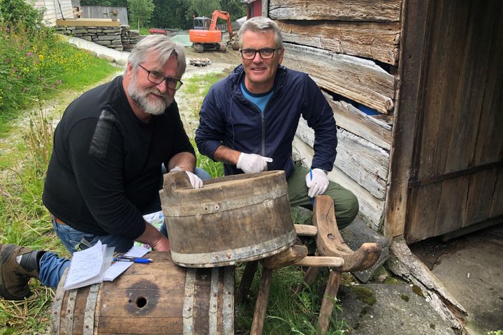 To menn arbeider med gammelt bryggeutstyr ved et trehus.