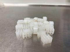 Små, hvite plastbiter med hullete struktur på en metalloverflate.