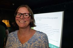 En kvinne med briller smiler foran en skjerm med en presentasjon.