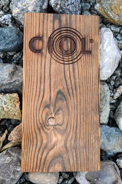 Kort rektangulær treplate med logoen "CIOL®" på overflaten, liggende på et underlag av steiner.