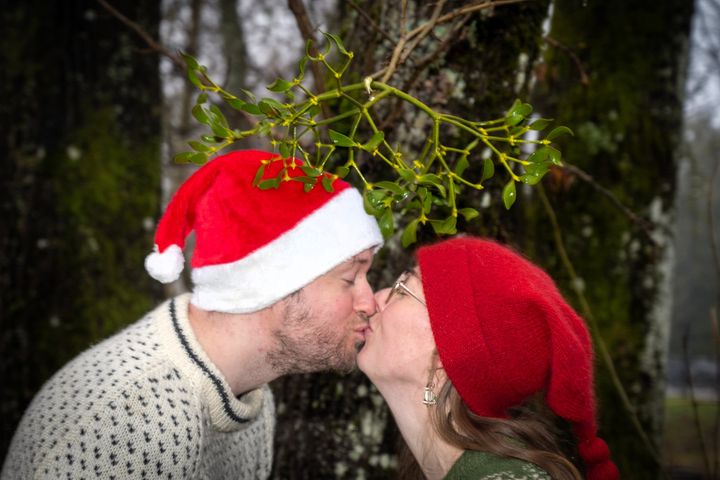 Et par kysser under misteltein. Begge har på seg nisseluer.