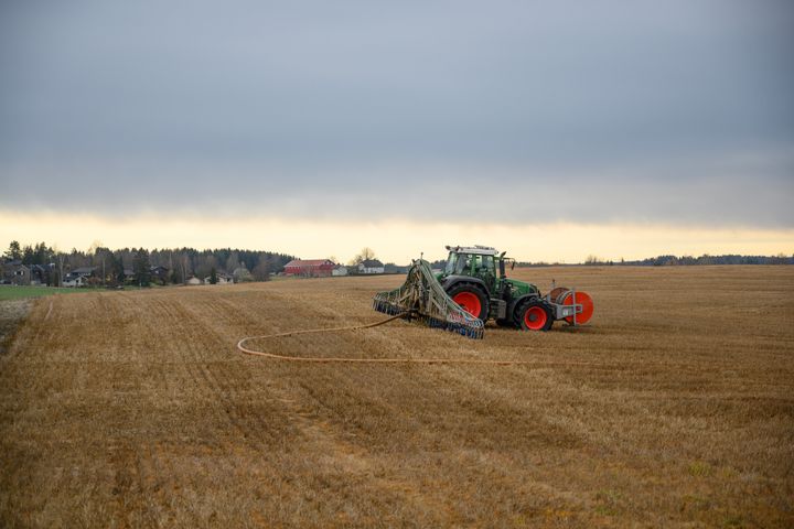 En traktor med slangespreder arbeider på et jorde under en overskyet himmel.