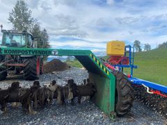 En grønn kompostvender ved siden av en rød og blå ugrasharv på grusvei.