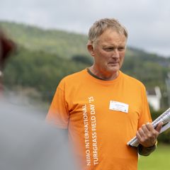 En person i en oransje T-skjorte står utendørs med notater i hånden.