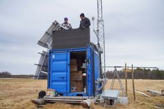 To personer installerer utstyr på en blå container i et åpent felt.