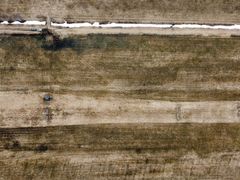 Dronebilde av et forsøksfelt i Pasvik med lange, rektangulære jordflekker og noen snødekte områder.