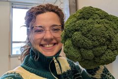 Kvinne smiler og holder en stor broccoli.