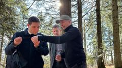 Bilde av tre personer i skogen som studerer en gjenstand.